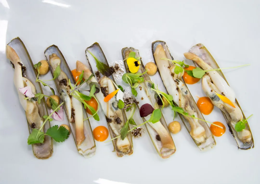 Razor clams with orange sauce and microgreens on a plate